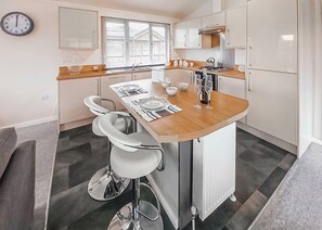 A compact kitchen with a central island, a sink, and a stove. There are two bar stools and a clock on the wall.