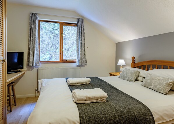 A bedroom with a bed, a TV, a window with curtains, a bedside lamp, and a radiator.