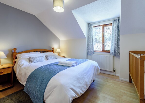 Une chambre à coucher avec un lit en bois, une table de chevet, une fenêtre avec des rideaux, un radiateur et un berceau en bois.