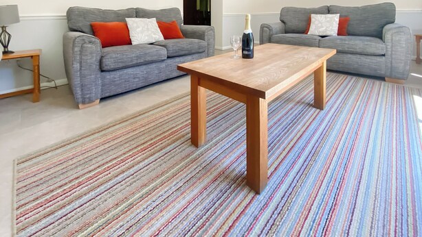 Ein modernes Wohnzimmer mit zwei grauen Sofas, einem Holztisch und einem farbenfrohen Streifen Teppich.