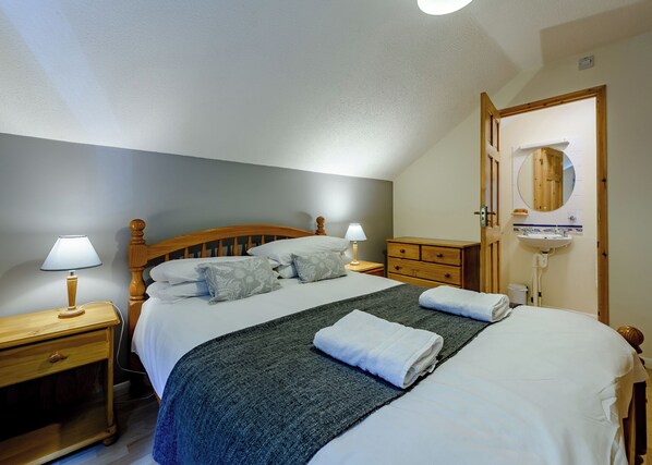 Une chambre à coucher comprenant un lit, des tables de chevet, une commode, un miroir et une salle de bain avec un lavabo.