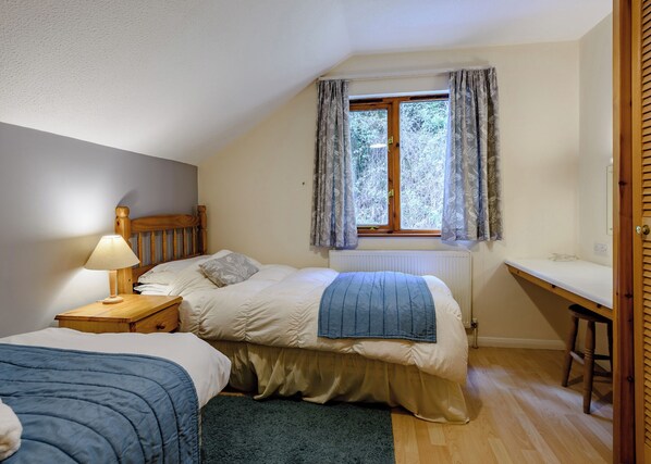Une chambre à coucher comprenant un lit, une table de chevet, une lampe, une fenêtre avec des rideaux, un radiateur et un petit bureau.