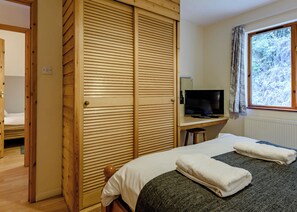 Une chambre à coucher avec un lit, une télévision, une armoire en bois et une fenêtre donnant sur les arbres.