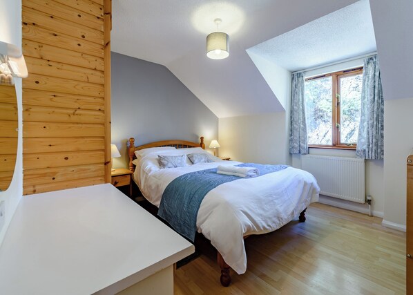 Une chambre avec un plafond en bois, un lit avec une literie blanche, une table de chevet, une fenêtre avec des rideaux et un radiateur.