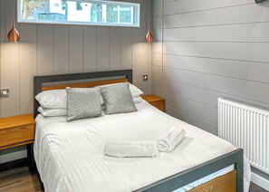 Ein ordentlich bezogenes Bett mit Kissen, ein Nachttisch aus Holz, ein kleiner Holztisch und ein Fenster mit Blick auf Gebäude.