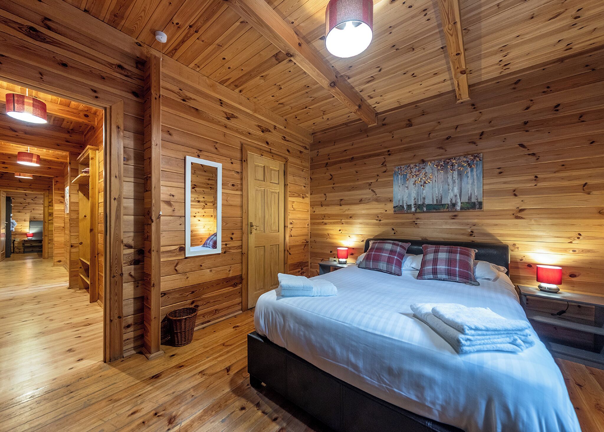 Quarto estilo cabana de madeira, com uma cama, mesas de cabeceira, um espelho e um quadro na parede.
