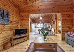 A wooden cabin interior with a TV, dining table, and a flower vase.