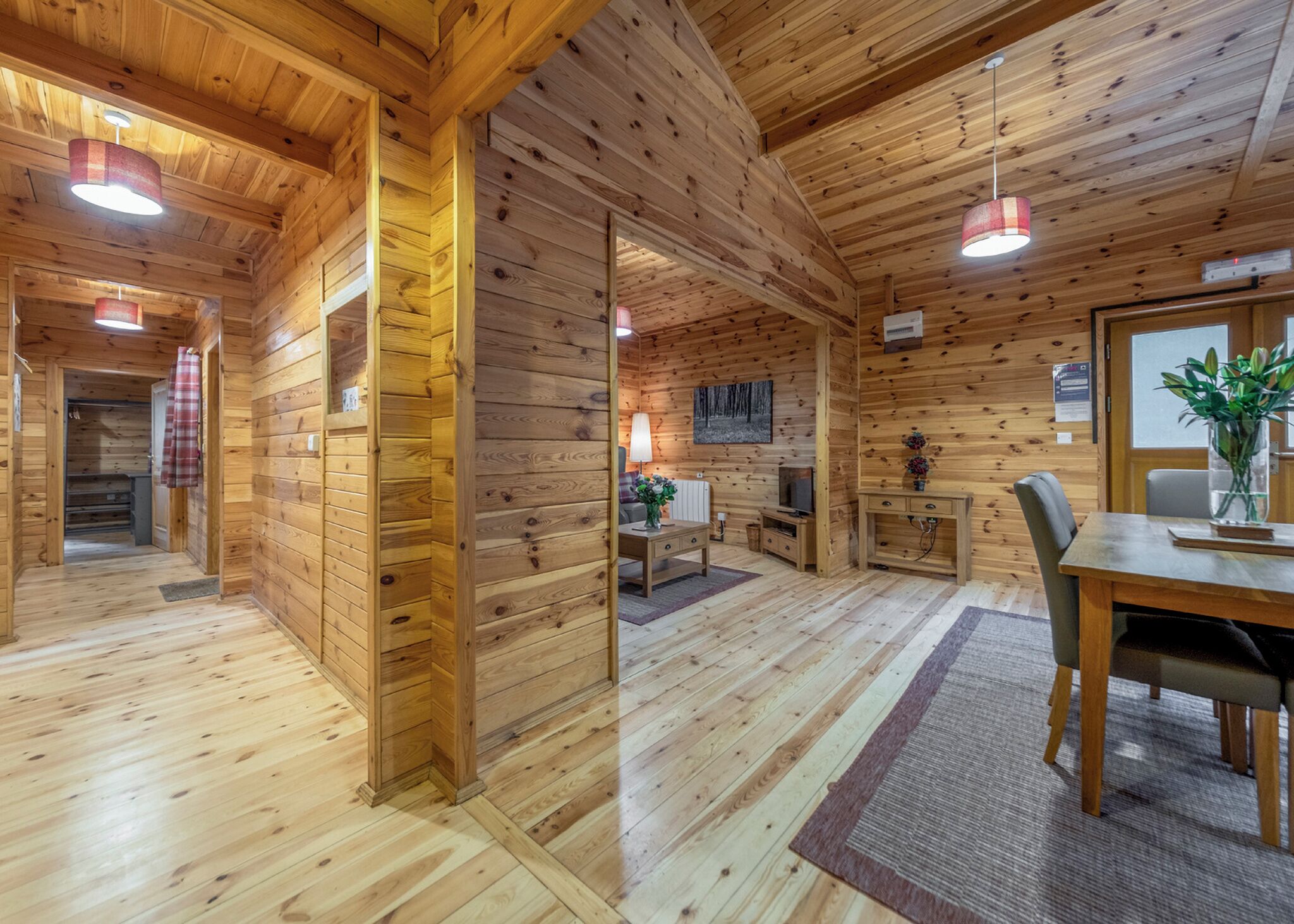 A wooden cabin interior with a dining area, a kitchen, and a living space.