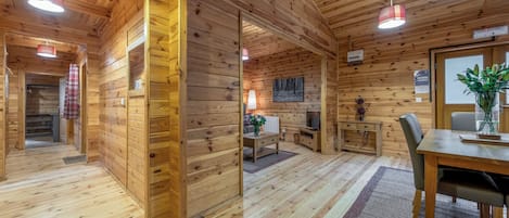 A wooden cabin interior with a dining area, a kitchen, and a living space.
