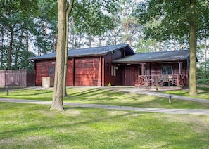 A rustic cabin with a porch, surrounded by trees and a fenced yard.
