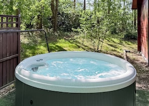 A hot tub in a backyard with a wooden fence, trees, and a shed.