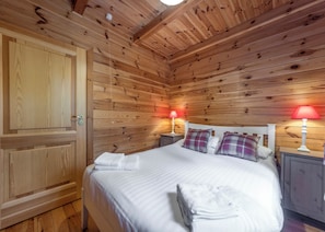 Um quarto de madeira com uma cama, duas mesas de cabeceira e uma porta.