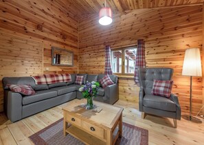 A wooden cabin interior with a sofa, armchair, and a small table with a vase of flowers. - Spacious lodge with modern styling features. (Ellesmere)