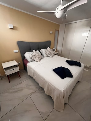 A modern hotel room with a neatly made bed, a bedside table with a lamp, and a ceiling fan.