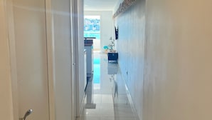 A hallway with a tiled floor, a white door on the left, and a wall with a decorative shelf. - Santa Ponsa Mallorca first line of sea - Aparthotel (Santa Ponça)