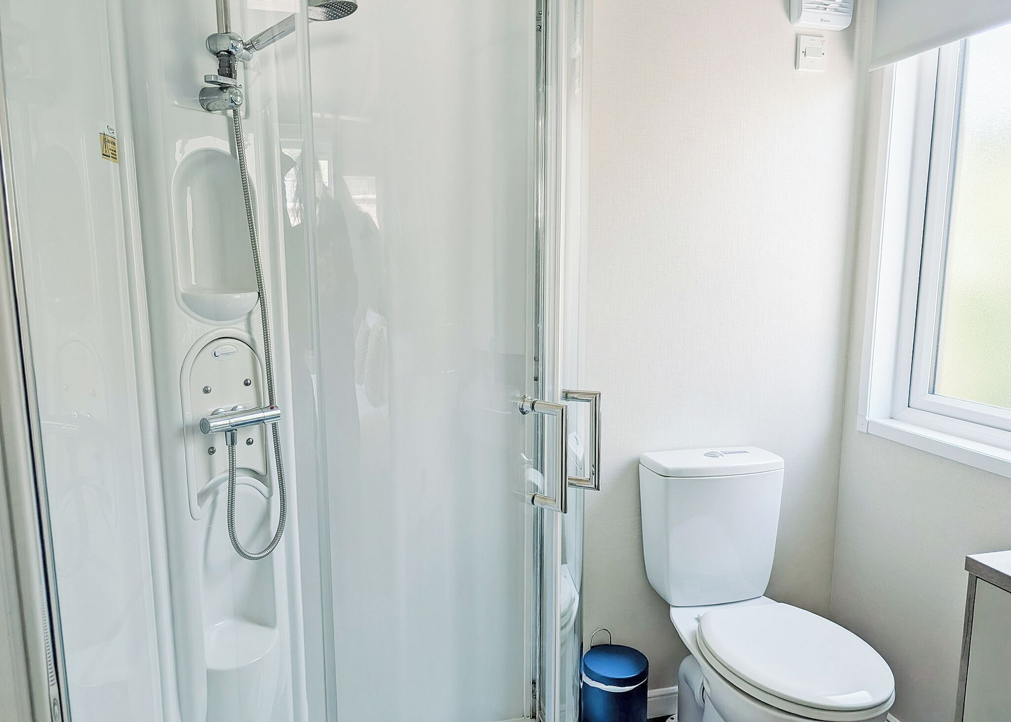 Een badkamer met een douchecabine van glas, een toilet en een raam.