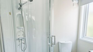 Ein Badezimmer mit Duschkabine aus Glas, Toilette und Fenster.