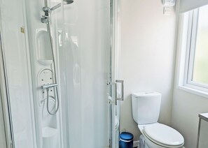 Et badeværelse med glasvæg omkring brusebad, toilet og et vindue.