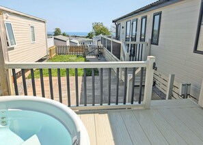 En terrasse med jacuzzi, trægelændere og udsigt til andre hytter.