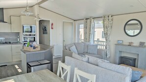 Eine moderne Küche mit Kochinsel, ein Essbereich mit Holztisch und ein Wohnzimmer mit Sofa und Kamin.