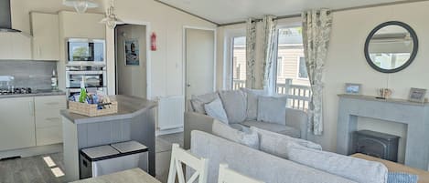Eine moderne Küche mit Kochinsel, ein Essbereich mit Holztisch und ein Wohnzimmer mit Sofa und Kamin.