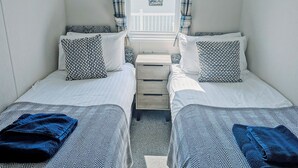 Ein Zimmer mit zwei Einzelbetten, jedes mit gemusterten Kissen und einem blauen Handtuch. Zwei Wandleuchten und ein kleiner Nachttisch aus Holz befinden sich zwischen den Betten.