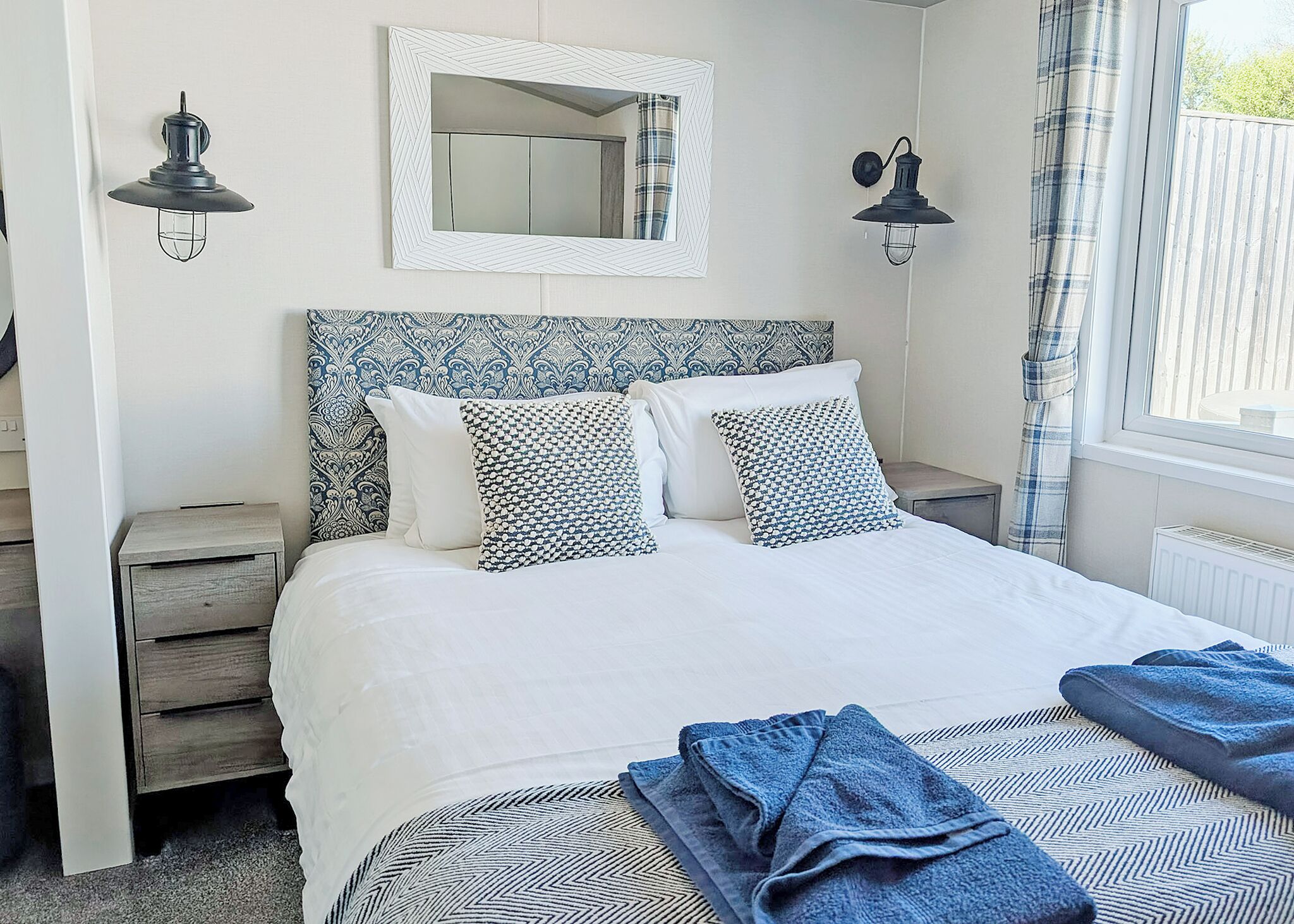 Een slaapkamer met een bed, twee nachtkastjes, een spiegel en een raam met gordijnen.