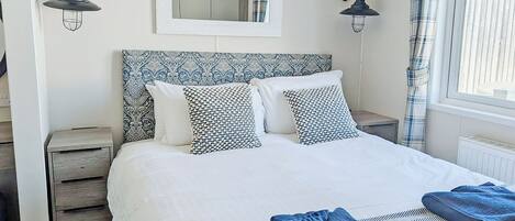 Un dormitorio con una cama, dos mesitas de noche, un espejo y una ventana con cortinas.