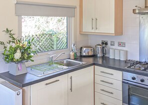 Une cuisine moderne avec des meubles blancs, un évier en acier inoxydable, un grille-pain, une bouilloire et une cuisinière à gaz.
