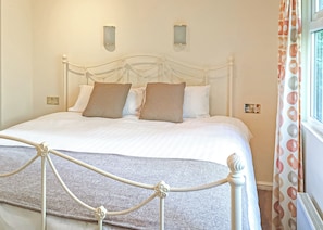 A neatly made bed with a white headboard, two wall-mounted light fixtures, and a window with patterned curtains.