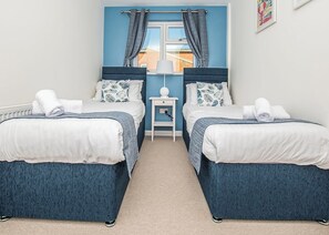 A room with two beds, a nightstand, a lamp, and a window with curtains.