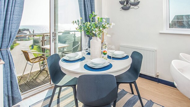 Een eetgedeelte met een ronde tafel, stoelen en een vaas met bloemen.