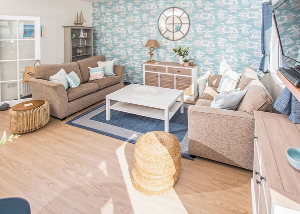 A living room with a sofa, coffee table, and a decorative wall with a nautical theme. - Ladram Seaview Apartment (Budleigh Salterton)