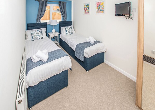 A hotel room with two beds, a small table, a TV, and artwork on the wall.