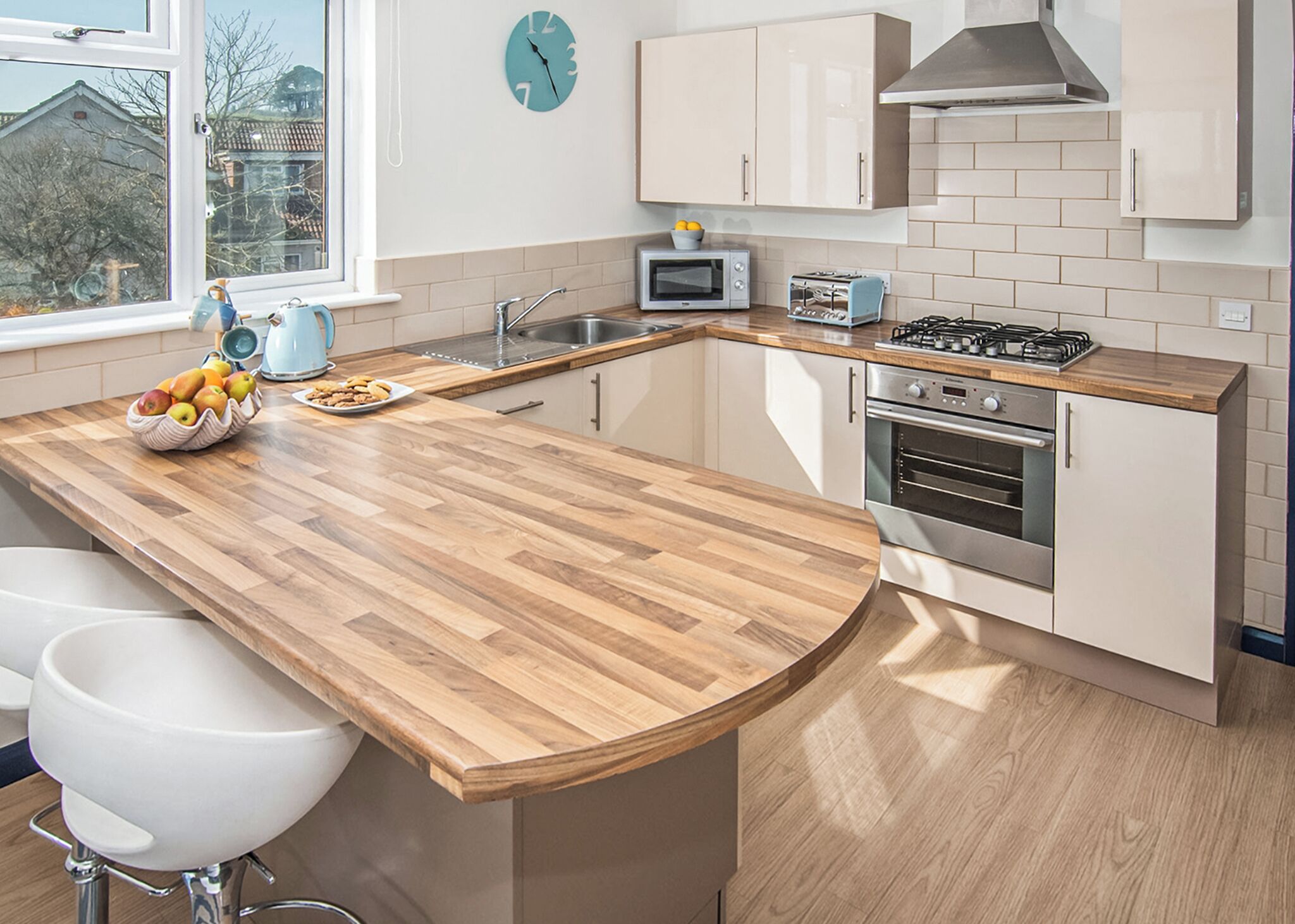 A modern kitchen with a wooden island, stainless steel appliances, and a view of the outside.