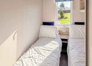 A small, single-bed room with a window, a bedside table, and a power outlet. - York Supeior 3 Caravan (Thirsk)