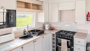 A compact kitchen with a stove, sink, and a window overlooking a garden. - York Supeior 3 Caravan (Thirsk)
