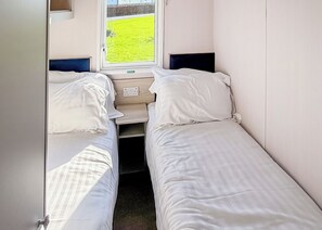 A small, single-room accommodation with two beds, a window with a view of a green field, and a bedside table.