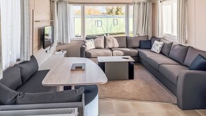 A modern RV interior with a sectional sofa, a small table, and a TV mounted on the wall. - York Supeior 3 Caravan (Thirsk)