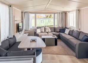 Un intérieur de camping-car moderne, avec un canapé modulable, une petite table et un téléviseur fixé au mur.