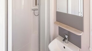 A bathroom with a glass shower door, a white sink, and a mirror above it. - York Supeior 3 Caravan (Thirsk)