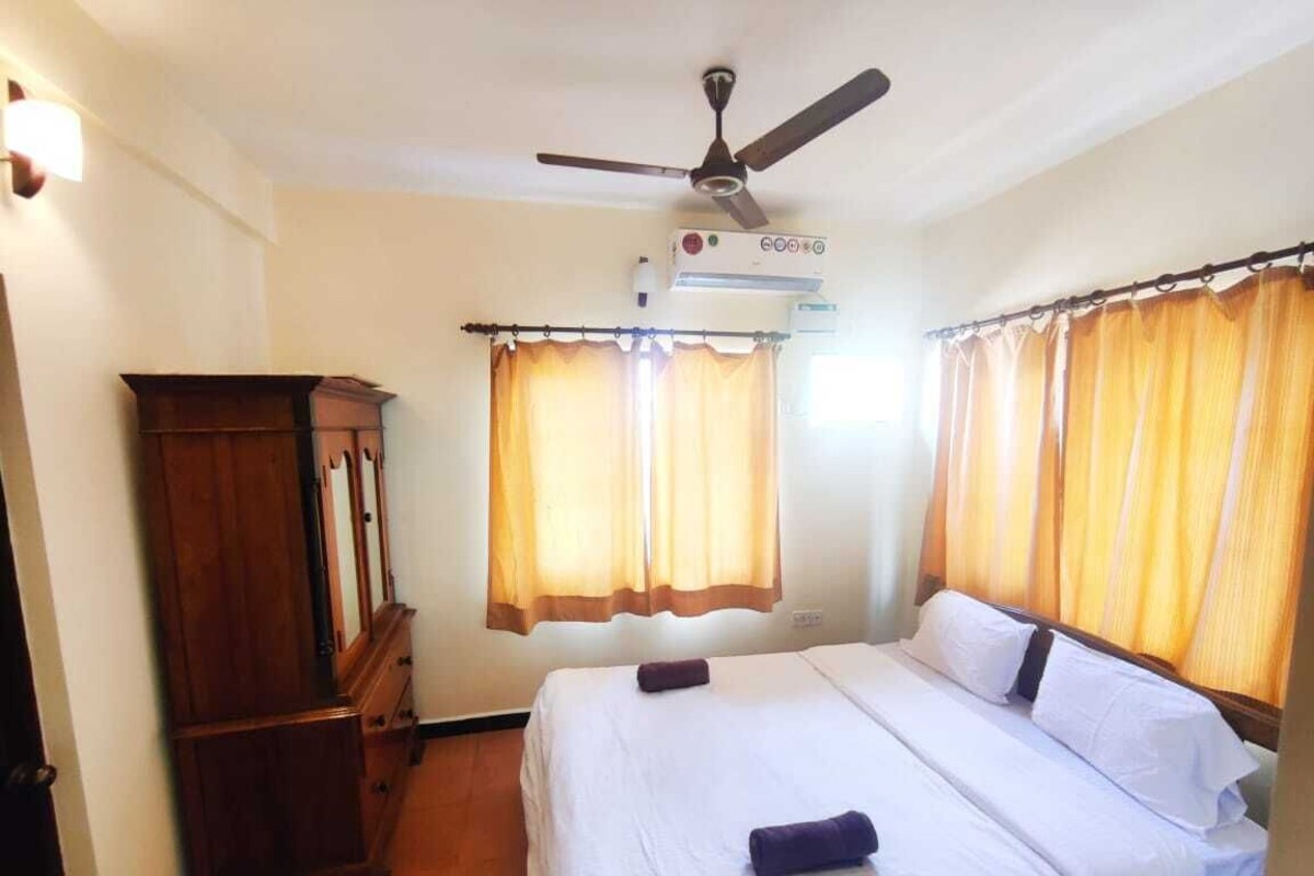 A hotel room with a bed, a ceiling fan, an air conditioning unit, and curtains.
