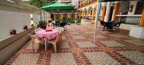 An outdoor patio area with tables and chairs, a patterned floor, and a green umbrella. - Veda Hotels & Villas (Marra)