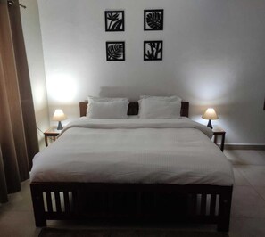 A hotel room with a large bed, two bedside lamps, and four wall art pieces. - Veda Hotels & Villas (Marra)