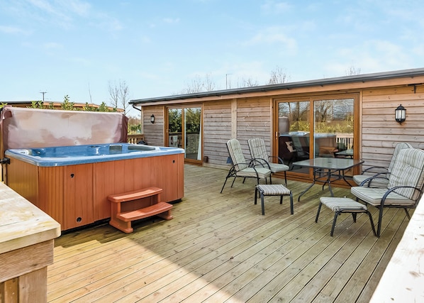 Eine Holzterrasse mit Whirlpool, Sitzgelegenheiten im Freien und einer Glasschiebetür zu einer überdachten Terrasse.