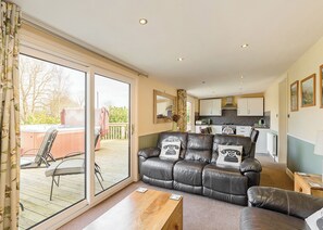 Una sala de estar con sofá, una mesa de centro de madera y un ventanal corredero que da a un área exterior con jacuzzi.