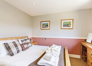 A bedroom with a bed, a bedside table, a bench, and two framed landscape paintings on the wall. - Luxury lodge with one double and one twin. (Pickering)