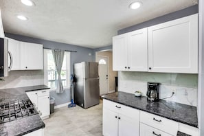 A kitchen with white cabinets, a stainless steel refrigerator, a gas stove, and a coffee maker. - The Columbus Garden Retreat | 5Beds One Level Home (Columbus)