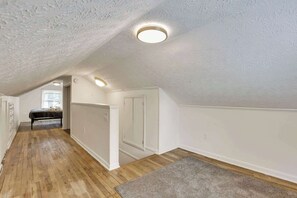 A narrow hallway with wooden flooring, white walls, and a ceiling with textured plaster.