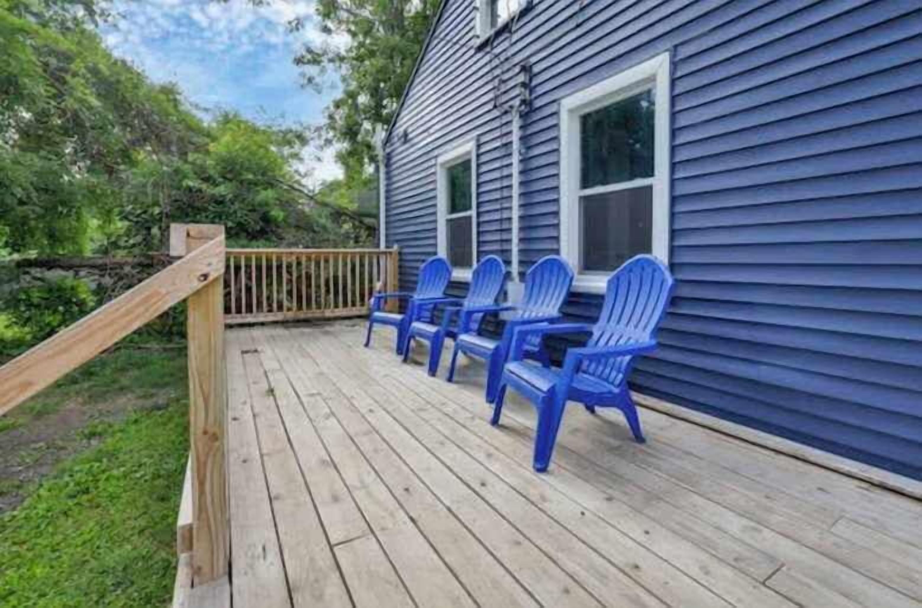 Une terrasse en bois avec des chaises bleues, une balustrade en bois et une maison aux murs recouverts de bardage bleu.